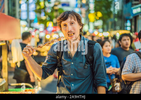 Junger Mann touristische Essen typisch koreanischen Street Food auf der Walking Street von Seoul. Würzig fast food einfach gefunden bei Koreanischen martket, Seele Korea Stockfoto