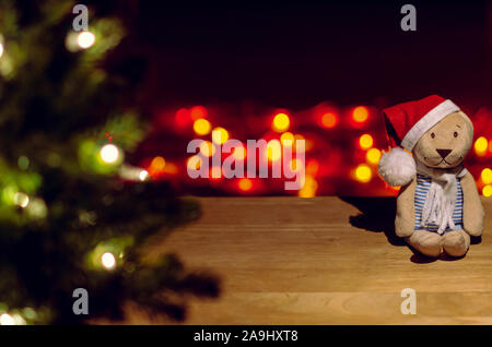 Weihnachtsmann Teddy sitzt auf Holztisch mit Weihnachtsbaum und bunten bokeh Lichter Hintergrund. Stockfoto