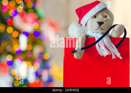 Santa Teddybär in Einkaufstasche mit unscharfen Fokus der bunten Weihnachtsbaum für Urlaub Dekoration Hintergrund. Stockfoto