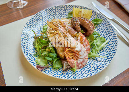 Gemischte gegrillte Meeresfrüchte einschließlich Thunfisch Steak und Schrimps Tintenfisch und Salat serviert auf einem modernen gedeckten Tisch Stockfoto