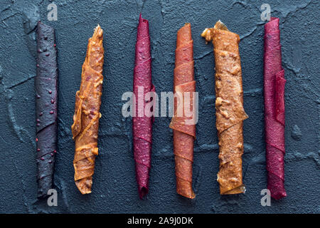 Süße püriertes Obst Roll-up pastila. Hausgemachte Obst Leder von Apfel, Aprikose, Erdbeere und Heidelbeere auf schwarzem Hintergrund. Obst rollen. Getrocknete Früchte. Stockfoto
