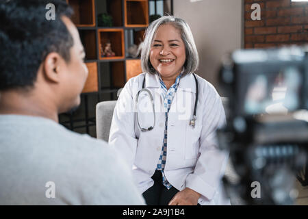 Lächelnd Arzt im Gespräch mit dem Patienten und die Aufnahme mit Kamera Stockfoto
