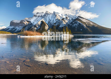 Schneebedeckte Bergspitzen-Landschaft mit niedriger Wolke, die sich in ruhigem Wasser widerspiegelt. Wunderschöner Lake Minnewanka, Banff National Park, Alberta, Kanadische Rockies Stockfoto