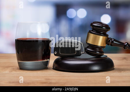 Autoschlüssel und Hammer über markante Block in der Nähe von Glas Alkohol im Gerichtssaal Stockfoto