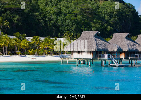 Ein Blick von der blauen tropischen Meer von ​​Authentic traditionellen polynesischen Häusern mit einem Strohdach über dem Wasser und einen Sandstrand mit Palmen ein Stockfoto