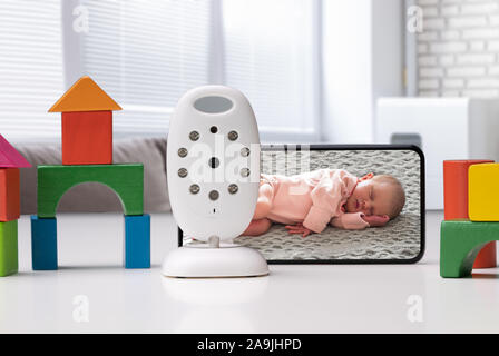 Bunte Spielzeug Häuser angeordnet in der Nähe von Mobiltelefon mit Baby Bild und drahtlose Kamera Stockfoto