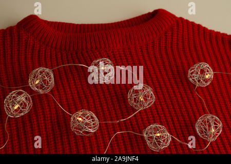 Rot gestrickt Jumper Verlegung auf weiße Oberfläche. Lichter von spreciral Formen. Neues Jahr und Weihnachten Konzept. Trendige Farben. Stockfoto