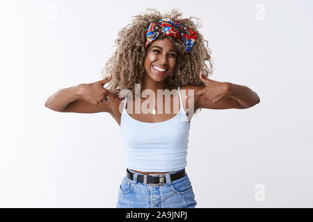 Stolz und glücklich, erfreut sich attraktive african-american blonde lockige blonde junge Frau mit Haarband, zeigen sich selbst prahlerisch, Gefühl hap Stockfoto