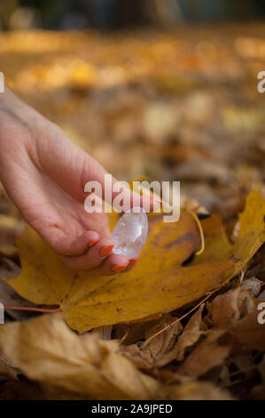 Weibliche hand mit orange Maniküre Holding transparent violett Amethyst yoni Ei für vumfit, imbuilding oder Meditation auf gelbem Laub Hintergrund Stockfoto