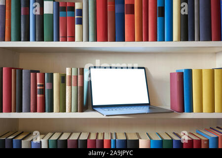 Laptop mit leerer Bildschirm im Bücherregal mit bunten Buch deckt Stockfoto