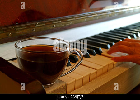 Tasse heißen Kaffee auf dem Klavier mit verschwommenen Pianist Hand im Hintergrund Stockfoto