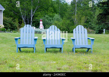Drei grauen Adirondack Stühle aufgereiht auf einem Rasen mit einem Leuchtturm Skulptur im Hintergrund. In Maine, USA. Stockfoto