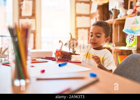 Schöne afrikanische amerikanische Kleinkind spielen mit Dinosaurier Spielzeug auf dem Schreibtisch im Kindergarten Stockfoto