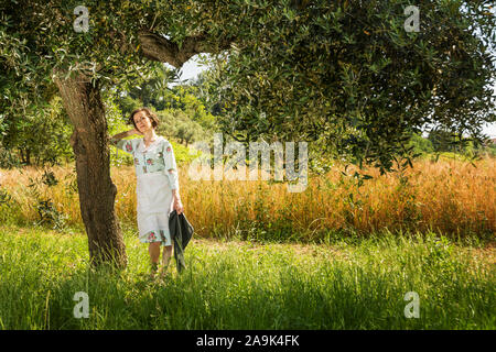 Frau in 40 die Kleider unter einem Olivenbaum in der Landschaft der Abruzzen mit einem Feld von Weizen im Hintergrund Stockfoto