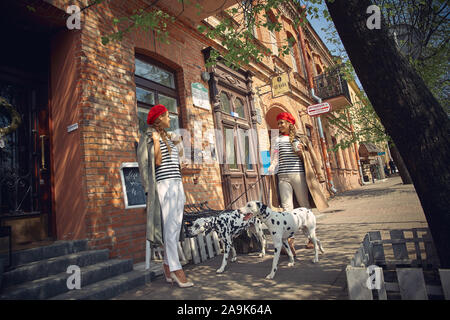 Zwei Mädchen in roten Barette sind Spaziergänge durch die Stadt mit Hunden der Dolmatian Rasse. Stockfoto