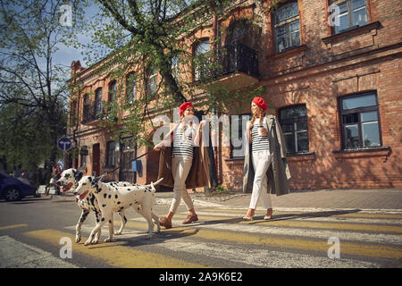 Zwei Mädchen in roten Barette sind Spaziergänge durch die Stadt mit Hunden der Dolmatian Rasse. Stockfoto