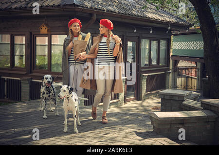 Zwei Mädchen in roten Barette sind Spaziergänge durch die Stadt mit Hunden der Dolmatian Rasse. Stockfoto