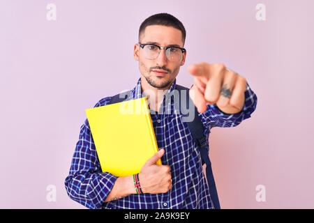 Junge hübsche Studentin Mann hält ein Buch über isolierte Hintergrund zeigt mit dem Finger auf die Kamera und an Sie, Hand unterzeichnen, positiv und zuversichtlich ge Stockfoto