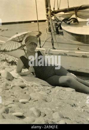 Eine Frau im schwarzen Badeanzug mit Strand und Sonnenschirm Stockfoto