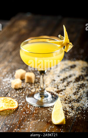 Gelbe tropischen Cocktail in einem eleganten Glas auf einer hölzernen Tresen. Rohrzucker ist neben dem Glas. Platz für Text Stockfoto