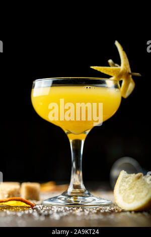 Gelbe tropischen Cocktail in einem eleganten Glas auf einer hölzernen Tresen. Rohrzucker ist neben dem Glas. Platz für Text Stockfoto