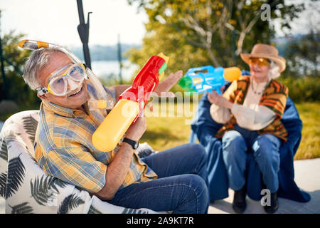 Lustigen Urlaub. lächelnd Senior paar Spielen mit Wasser Pistole Stockfoto