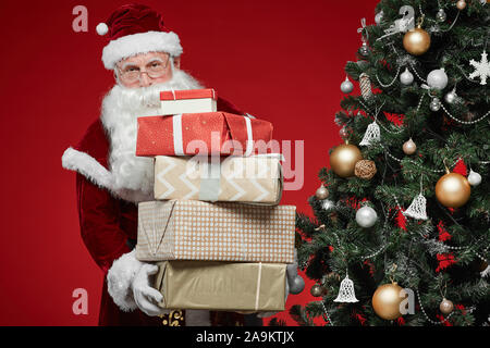 Portrait von Santa Claus mit weißen Bart stehen in der Nähe der Weihnachtsbaum und die Stapel von Weihnachten, stellt in seinen Händen für Kinder Stockfoto