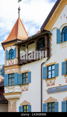 Schönes Haus mit gestrichenen Wänden, einem Turm und einem Turm, einen hölzernen Balkon und Fenster mit blauen Fensterläden in der Stadt Schwangau in Deutschland. Stockfoto