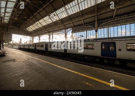 Der Personenzug parkte an einem Bahnsteig mit einer alten Dachkonstruktion an einem sonnigen Tag Stockfoto