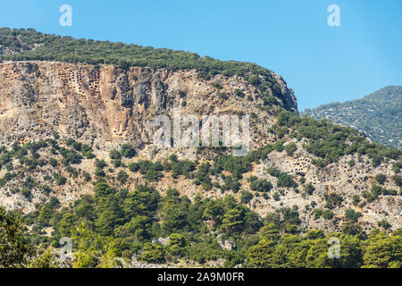 Crag mit Felsen gehauenen Gräbern hoch über den Ruinen der alten lykischen Stadt Pinara in der Türkei. Stockfoto