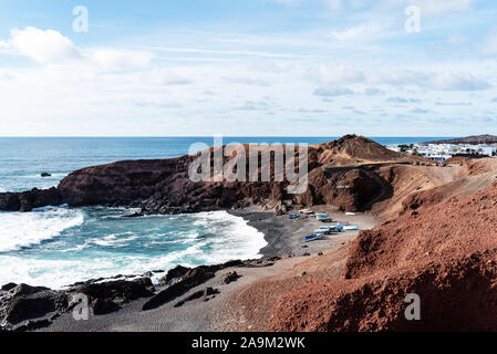 Kleine Boote auf dunklen Kieselstrand gegen die vulkanische Landschaft und dem blauen Meer auf Lanzarote, Kanarische Inseln Stockfoto