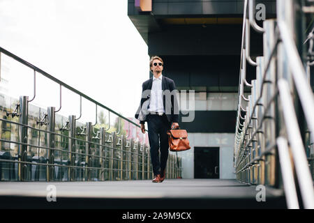 Der Chef im Anzug und Sonnenbrille mit einer Aktentasche in der Hand geht zu arbeiten Stockfoto