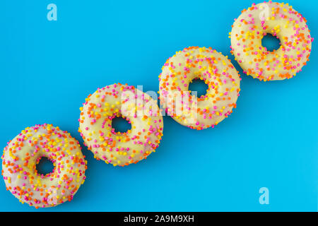 Eine Gruppe von hellen motley Donuts mit Streuseln auf blauem Hintergrund in abstrakten Stil. Ein Haufen von mehrfarbigen Donuts mit gelben Glasur. Positive creative Stockfoto