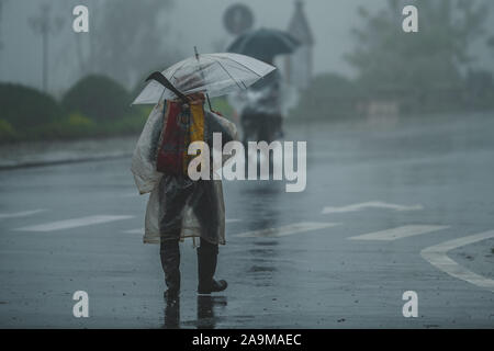 Sapa, Vietnam - 13. Oktober 2019: Ein alter asiatischer Mann unter einem Schirm geht weg von der Kamera im strömenden Regen in der kleinen Stadt Sapa Stockfoto