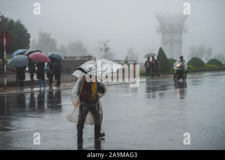 Sapa, Vietnam - 13. Oktober 2019: Ein alter asiatischer Mann unter einem Schirm geht weg von der Kamera im strömenden Regen in der kleinen Stadt Sapa Stockfoto