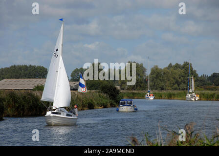 Sailng Yacht auf dem Fluss Thurne, Norfolk, England, gefolgt von kleinen Cruiser Stockfoto