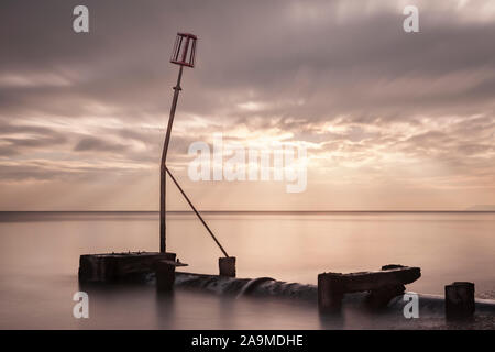 Abfluss Rohr und Marker auf Strand mit dämmerungs Sonnenstrahlen Streaming durch Wolken und lange Belichtung Unschärfe Flut, Bexhill-on-Sea, East Sus Stockfoto