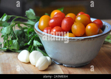 Cherry Tomaten, Knoblauch und Petersilie auf einem hölzernen Schneidebrett Stockfoto