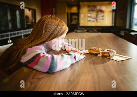 Junge Rothaarige Mädchen schauen sehnsüchtig auf Delicious Doughnuts Stockfoto