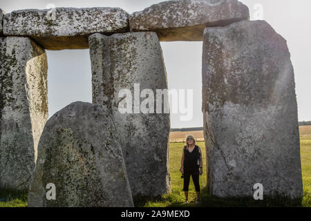 Touristische Frau, zwischen Steinen in Stonehenge in England an einem sonnigen Tag, um zu zeigen, wie groß sie sind, Stockfoto