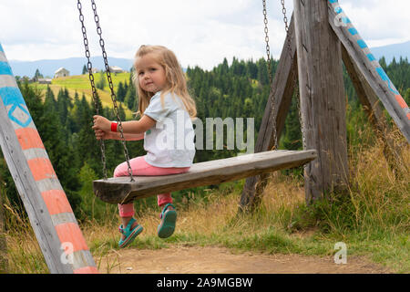 Kleines Mädchen schwingen auf Swing mit Bergblick auf Hintergrund Stockfoto