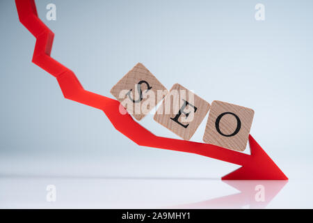 SEO Buchstaben auf Holzklötze auf Rot abnehmender Richtungspfeil gegen grauer Hintergrund Stockfoto