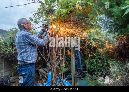 Mann mit einem Winkelschleifer im Garten arbeiten mit Funken fliegen. Abschneiden Gefährliche alte Nägel aus einem Post. Stockfoto