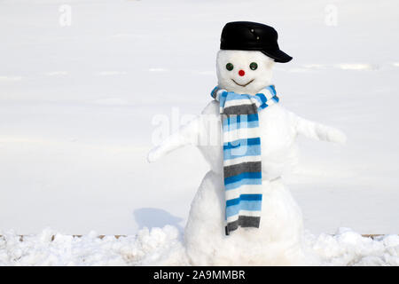 Ein Schneemann in schwarzer Mütze und blauem Schal steht im Winter, Weihnachten und Neujahr auf einer verschneiten Wiese, Unterhaltung und Sport. Stockfoto