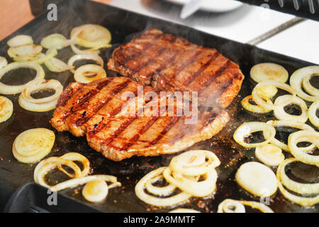 Zwei Schnitzel Steaks und Zwiebel in Scheiben schneiden, auf elektrischer Grill gegrillt, Rauch über Gegrilltes sichtbar Stockfoto