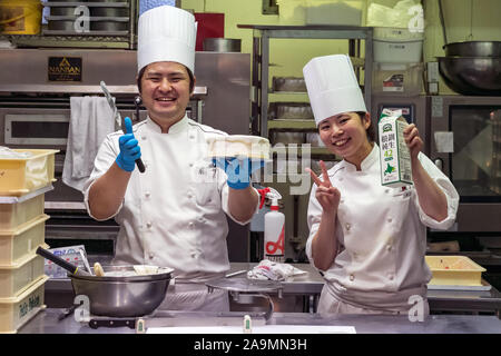 Zwei japanische Konditoren lächelnd Holding eine runde Kuchen ihres Stores Küche zu verzieren. Stockfoto