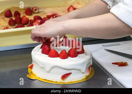 Weibliche Konditor Hände, die Dekoration einer Torte mit Erdbeeren. Stockfoto