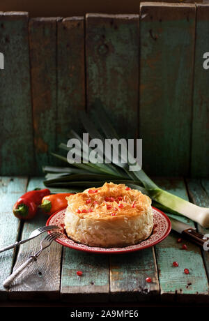 Griechisches Gebäck mit griescreme Teig. Hausgemachte Kuchen mit rohem Gemüse und Granatapfel Samen auf schäbigen blauen Hintergrund Kopie Raum. Low Key still life Stockfoto