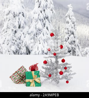 Weihnachten Geschenke unter künstlichen Lametta Baum im Freien mit schneebedeckten Bergen im Hintergrund. Aktuelles Foto geschossen im Winter Wildnis, nicht fake. Stockfoto