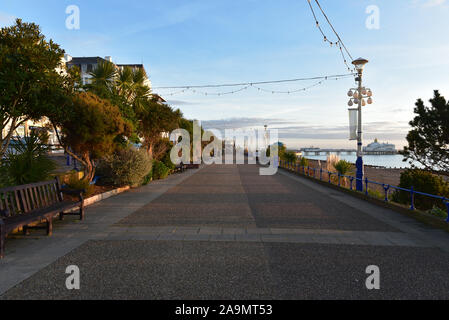 Leere Promenade mit Sitzbank, Lampenhalter und Eastbourne Pier im Abstand unter einer Dämmerung Himmel Stockfoto